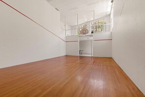 A squash court with a wooden floor, white walls, and a glass partition. - Luxury Waterfront Retreat with Private Pool (Daleys Point)