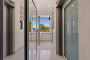 A modern corridor with glass doors leading to a balcony with a view of trees and a body of water. - Luxury Waterfront Retreat with Private Pool (Daleys Point)