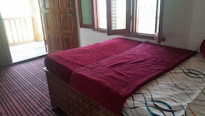 A room with a bed covered in a patterned blanket, a window with a view, and a door leading outside. - Homely Hills,6Km frm Nagtibba trek route (Mayani)