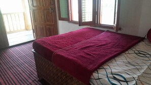 A room with a bed covered in a patterned blanket, a window with a view, and a door leading outside. - Homely Hills,6Km frm Nagtibba trek route (Mayani)