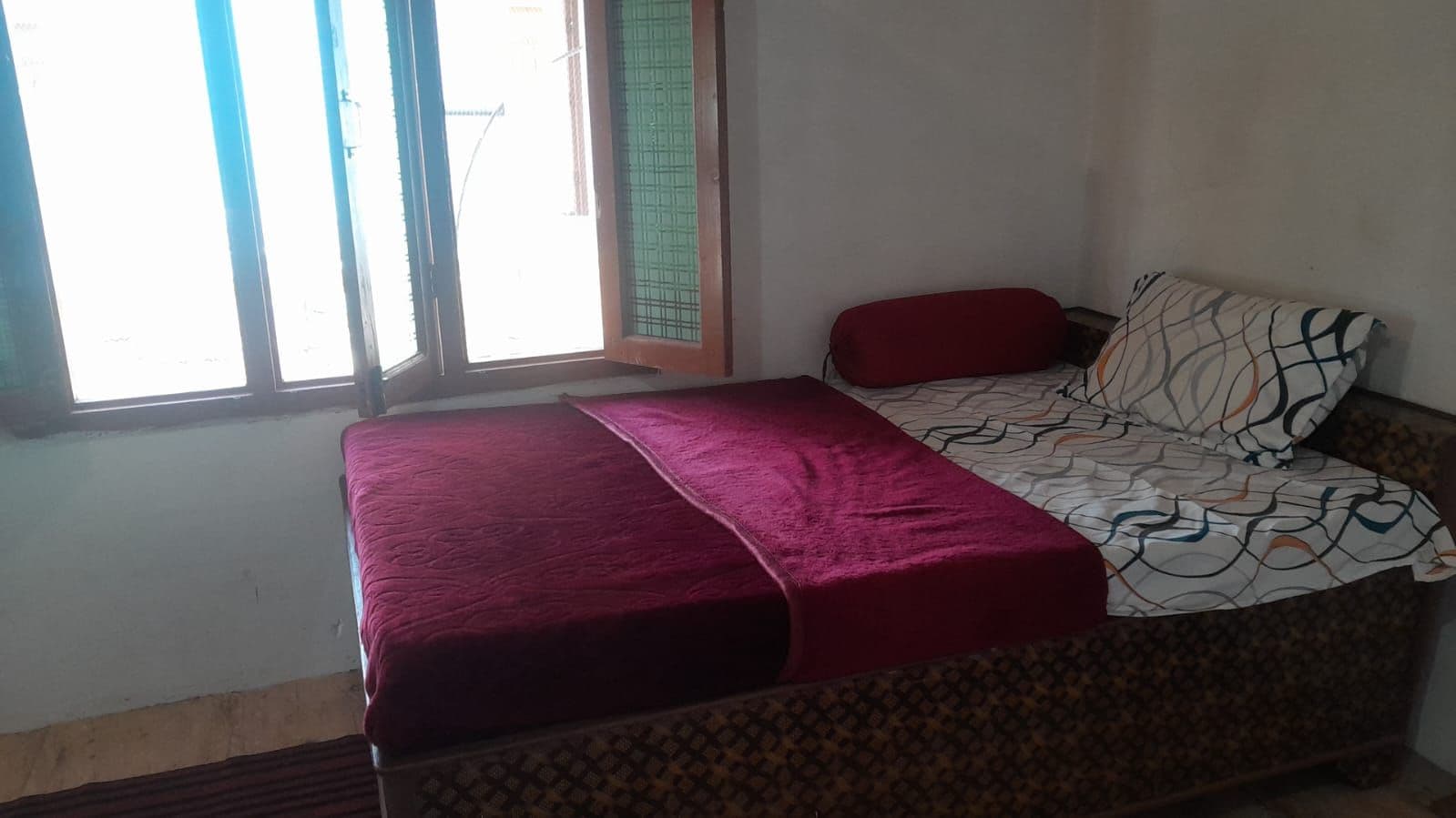 Una cama individual con colcha estampada y una manta roja.