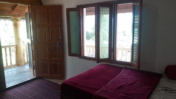 Una habitación con una cama, una puerta de madera y ventanas con vistas al exterior.