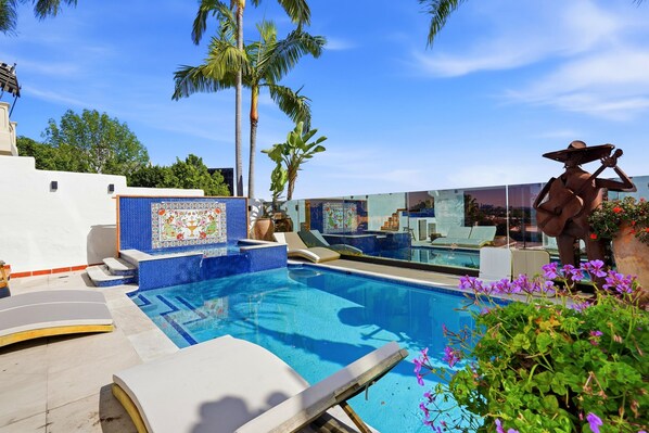 A swimming pool with a tiled edge, lounge chairs, and a statue.