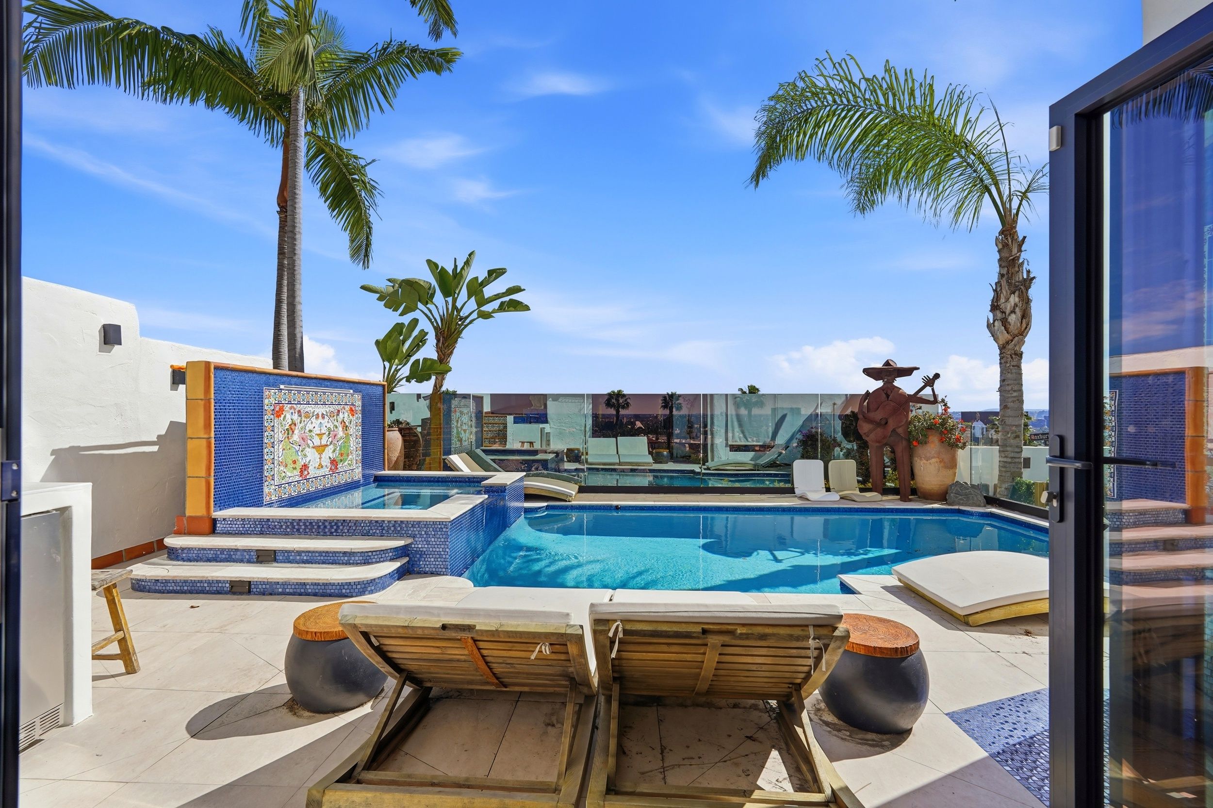 A pool area with lounge chairs, a tiled deck, and palm trees.