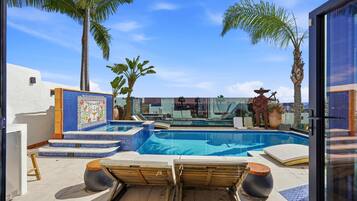 A pool area with lounge chairs, a tiled deck, and palm trees.