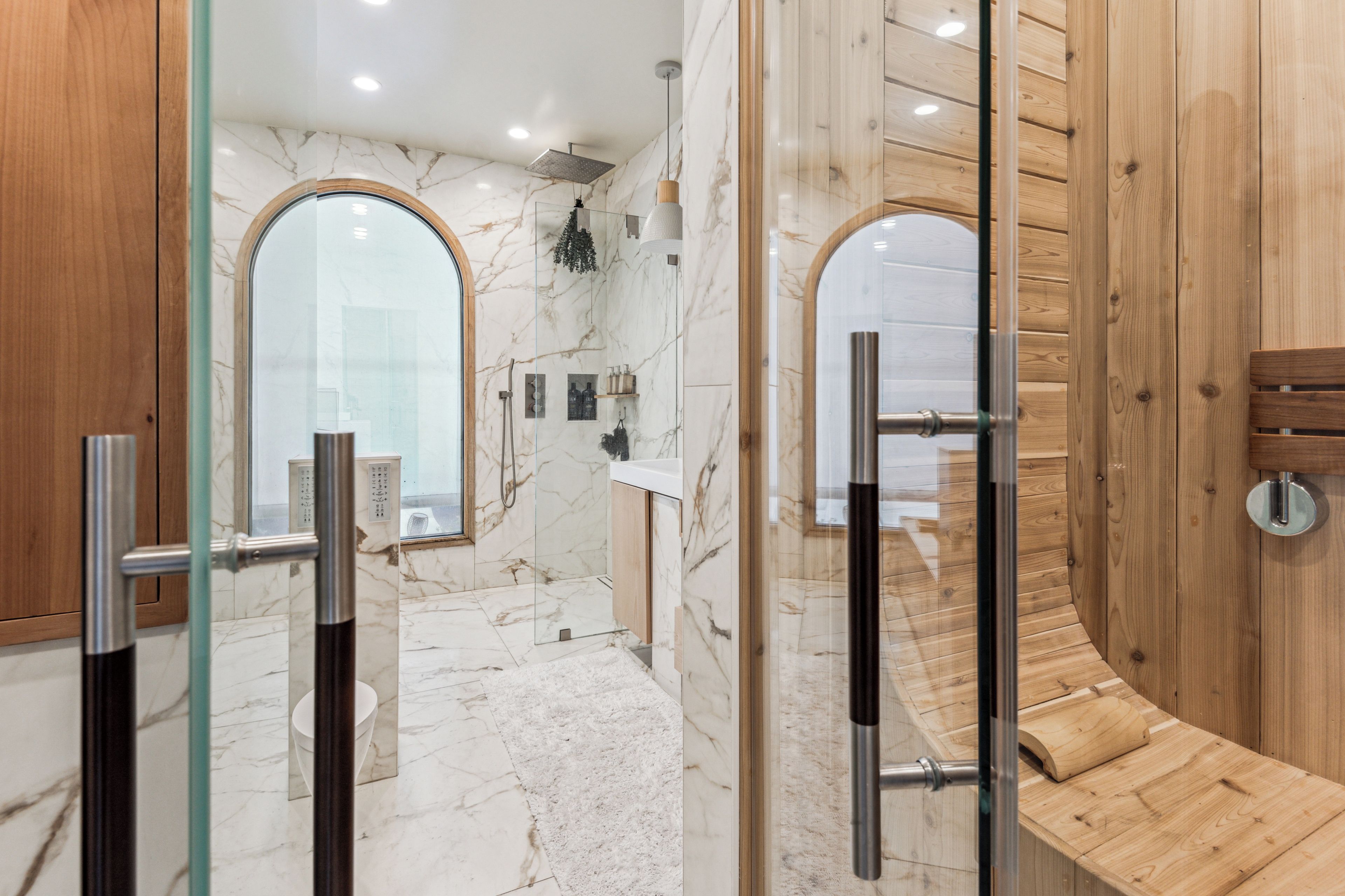 A modern bathroom with a glass-enclosed shower, marble walls, wooden accents, and a visible toilet.