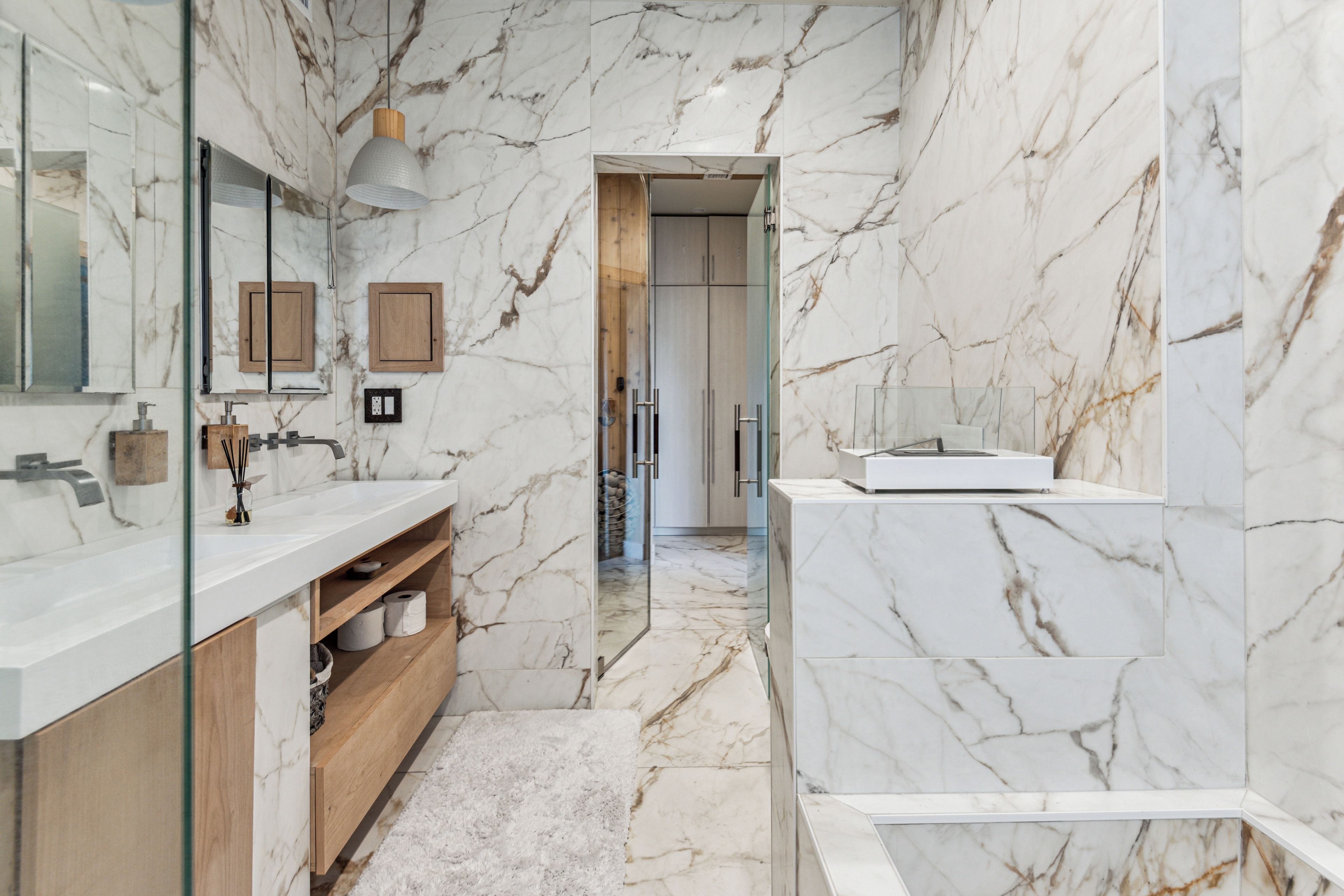 A modern bathroom with marble walls, a glass shower enclosure, and wooden cabinetry.
