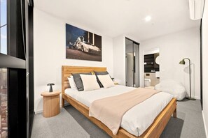 A modern bedroom with a large bed, a view of the city, and a painting of a car on the wall. - The Speakeasy · 3BR · Poker + Parking + Pool (Melbourne)