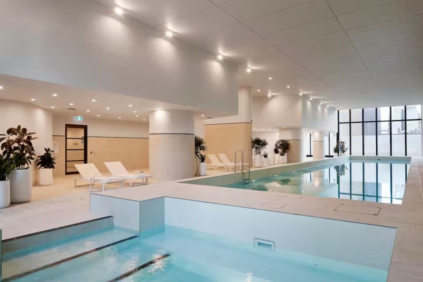 An indoor swimming pool with lounge chairs and potted plants.