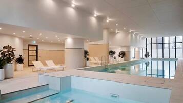 An indoor swimming pool with lounge chairs and potted plants.