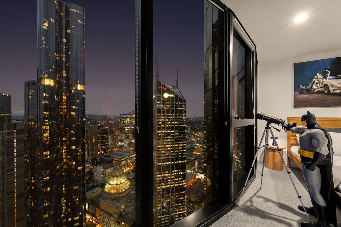 A high-rise room with a city view, a telescope, and a Batman action figure.