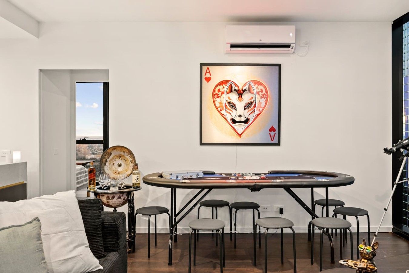 A room with a poker table, chairs, a sofa, and a framed playing card artwork on the wall.