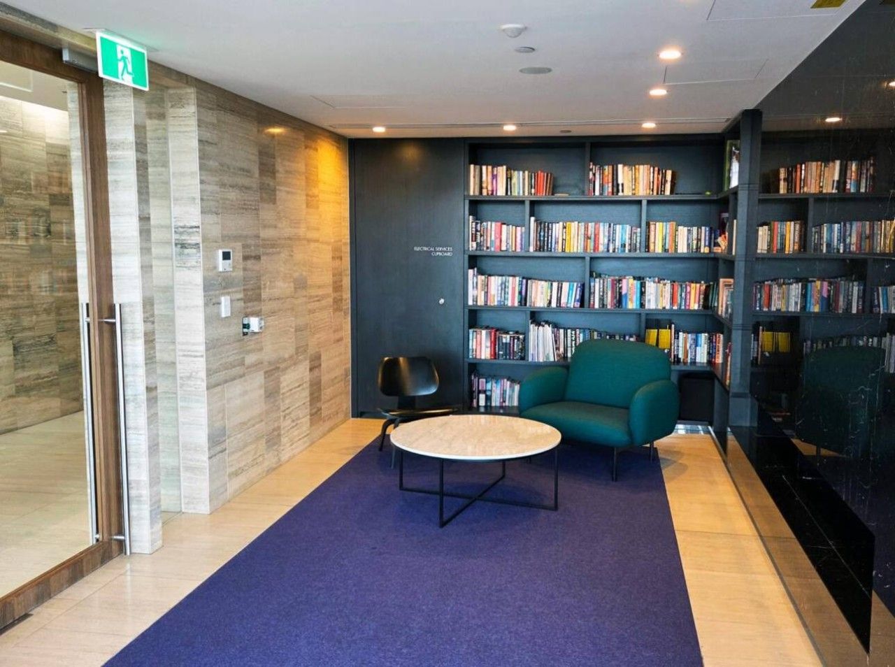 Een moderne bibliotheek met een blauw tapijt, een ronde tafel en een blauwgroene bank.
