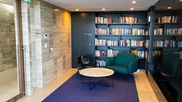 Een moderne bibliotheek met een blauw tapijt, een ronde tafel en een blauwgroene bank.