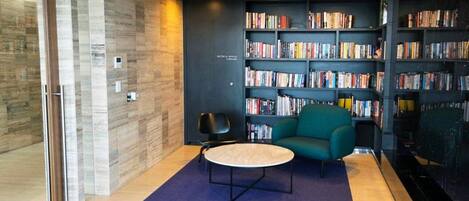 A modern library with a blue carpet, a round table, and a teal sofa.