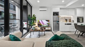 A modern living room with a sofa, a coffee table, and a TV. There is a kitchen area with a fridge and a microwave. - Rooftop Pool Views · Sleek 1BR on St Kilda Rd (Melbourne)