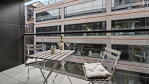 A modern balcony with a glass table, two chairs, a bottle of wine, and a small plant. - Rooftop Pool Views · Sleek 1BR on St Kilda Rd (Melbourne)