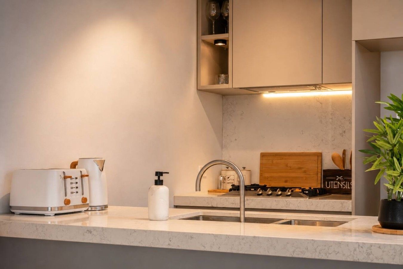 A modern kitchen with a marble countertop, a toaster, a soap dispenser, and a wooden cabinet above the sink.
