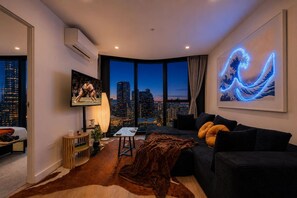 Ein modernes Wohnzimmer mit Blick auf die Stadt, einem an der Wand befestigten Fernseher und einer Neon-Wellen-Kunstinstallation.