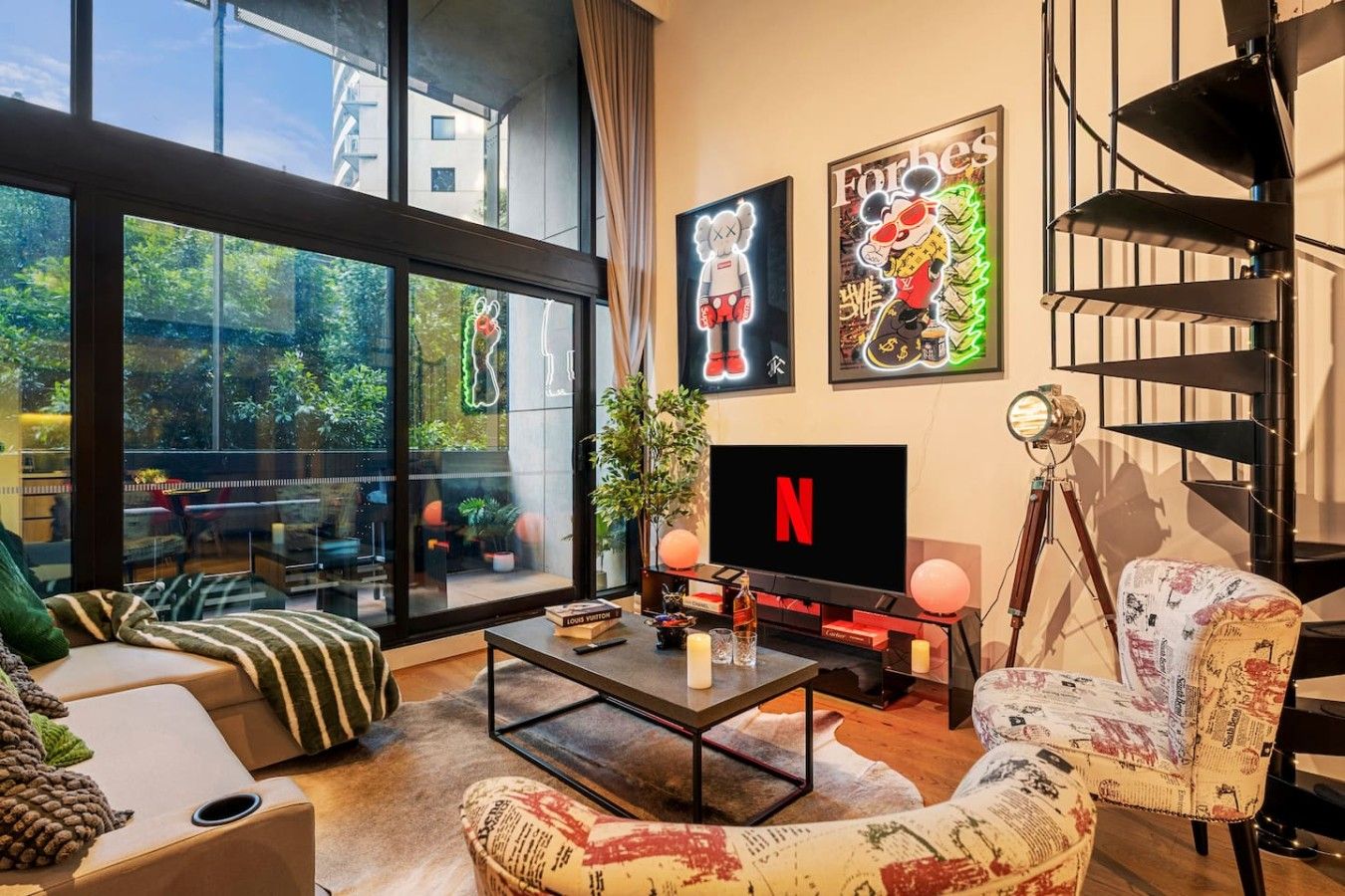 Ein modernes Wohnzimmer mit einem großen Fenster, einem Flachbildfernseher, einer Treppe und einem Couchtisch.