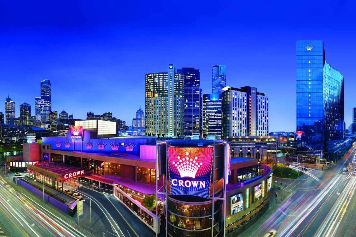 A cityscape with a prominent building featuring the 'Crown' sign, surrounded by high-rise buildings and busy streets.