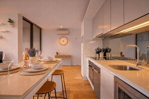 A modern kitchen with a central island, stainless steel appliances, and a dining area with a table set for a meal. - Golden Hour · 2BR · Level 42 Skyline + Pool (Melbourne)