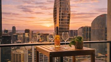 A table with a bottle and glasses, overlooking a cityscape at sunset.