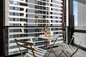 A modern interior with a balcony, a round table with a bottle and glass, and two chairs. - Designer 2BR · Heart of CBD · Pool + Free Trams (Melbourne)