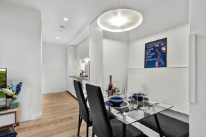 A modern dining area with a glass table, black chairs, and a blue poster on the wall. - Designer 2BR · Heart of CBD · Pool + Free Trams (Melbourne)