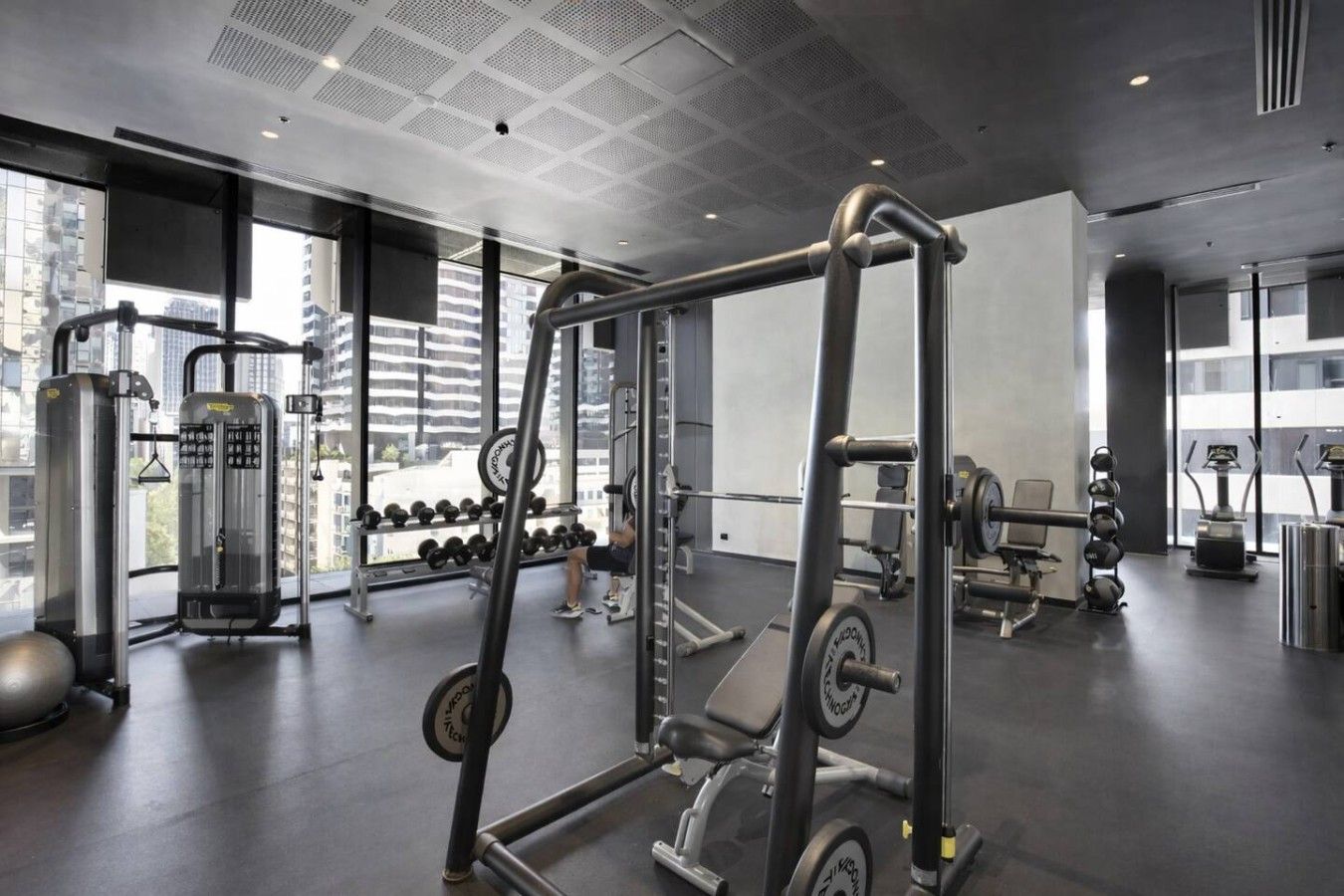 A modern gym with various exercise equipment, large windows, and a city view.