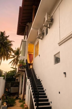 Un edificio blanco con una escalera negra que lleva a una puerta, rodeado de palmeras.