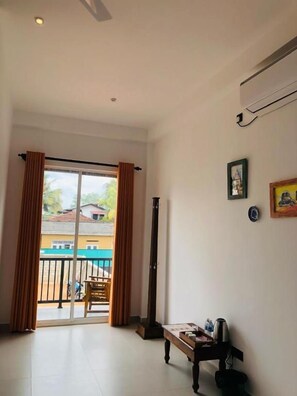 A room with a sliding glass door leading to a balcony, a small table with a chair, and a wall-mounted air conditioning unit.
