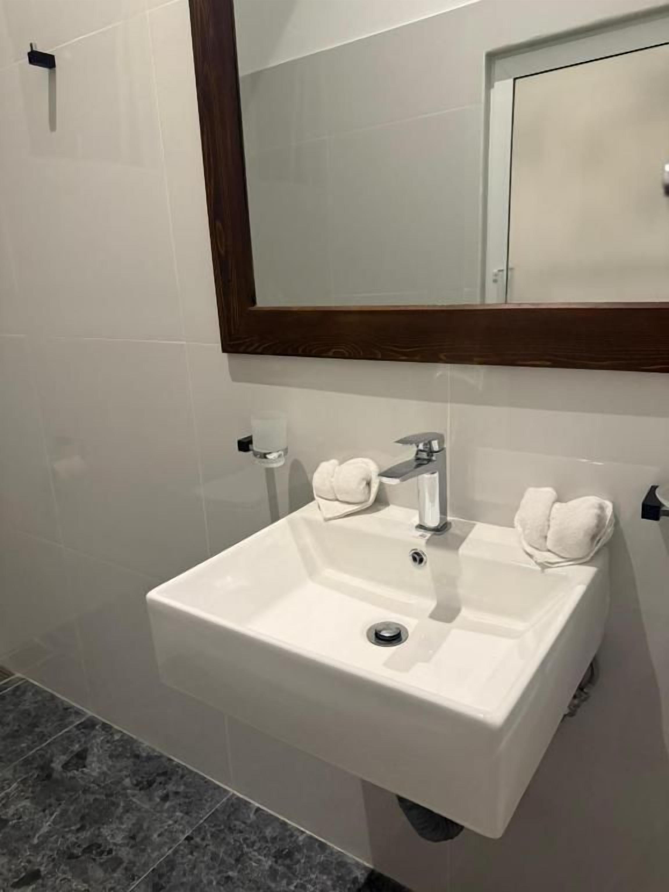 Un baño con lavamanos blanco, espejo y toallero.