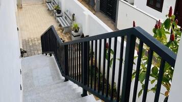 Un escalier avec une rampe noire menant à un espace extérieur abrité, aménagé avec des bancs et des plantes en pot.