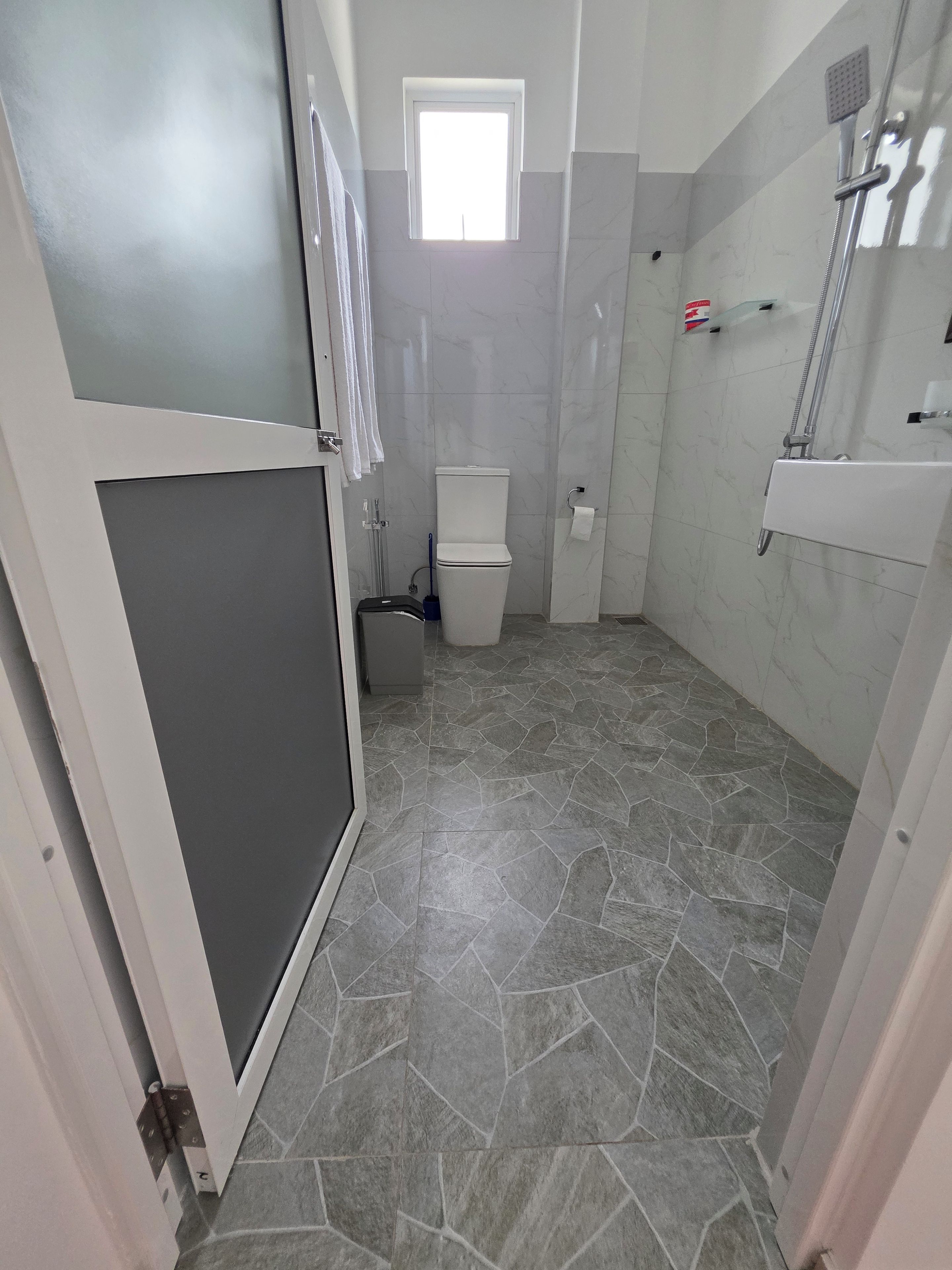 A bathroom with a toilet, shower, and a small window.