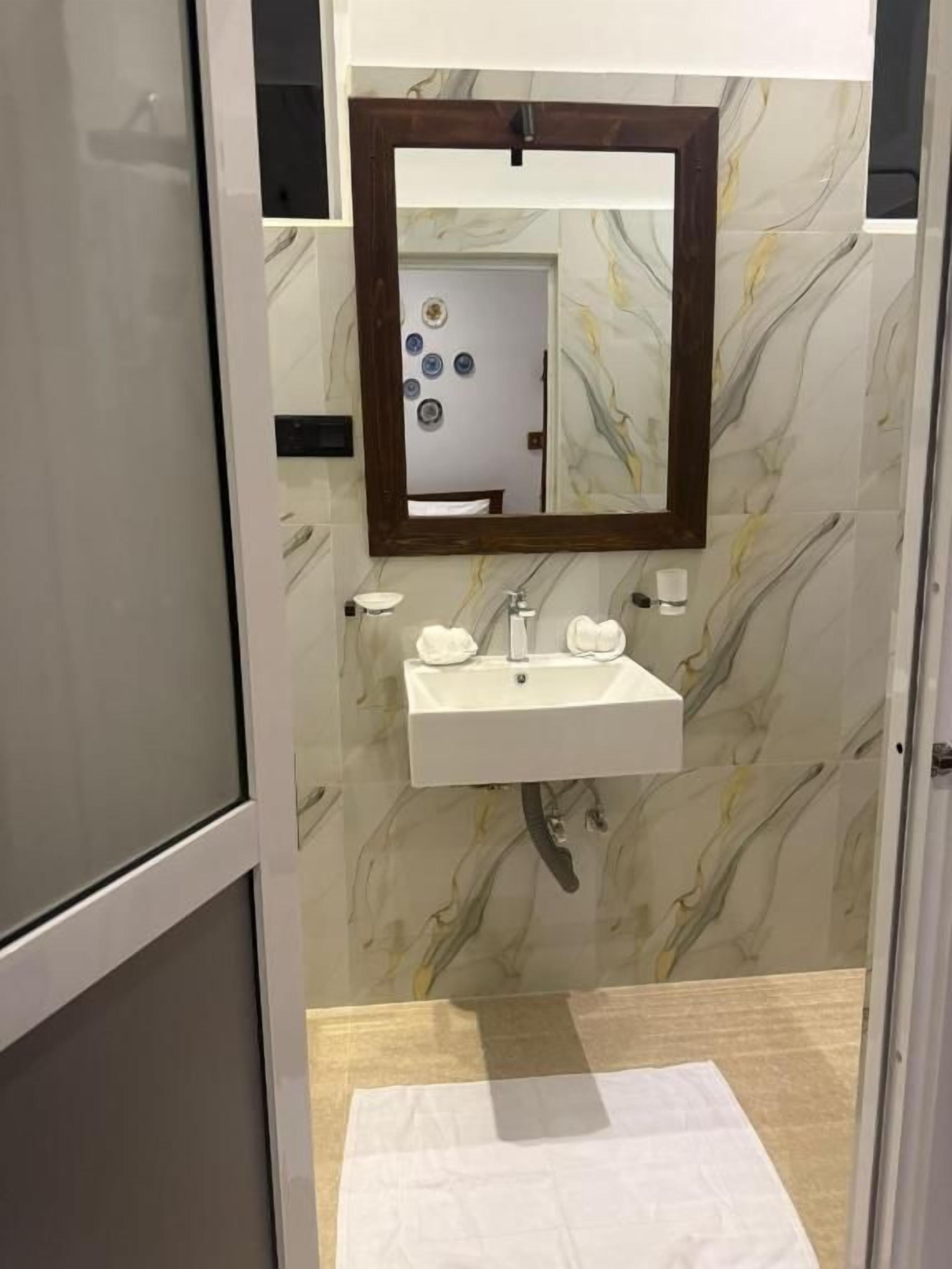 Un baño con pared de mármol, un lavabo blanco y un espejo con marco de madera.