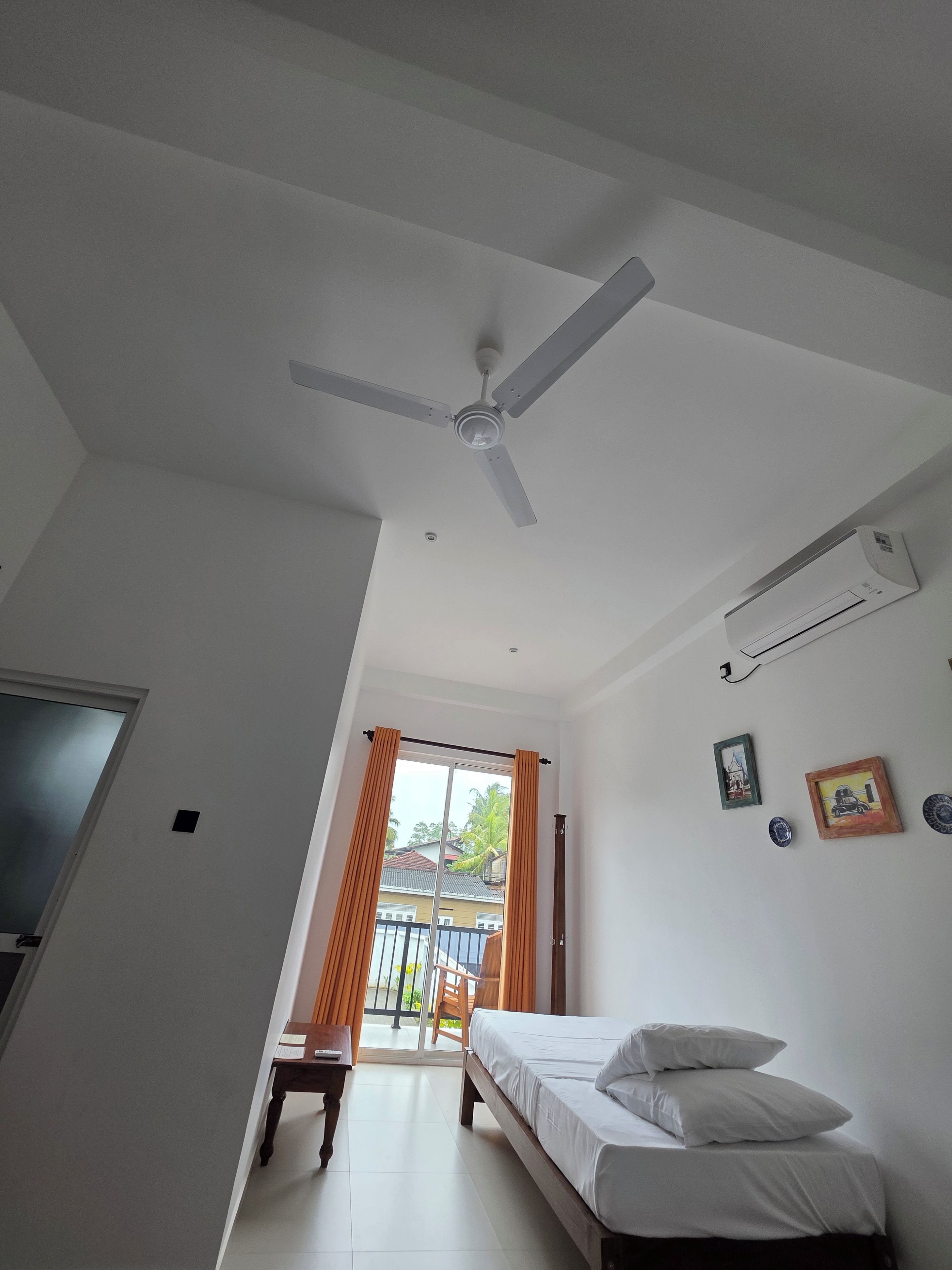 A bedroom with a bed, a ceiling fan, a window with curtains, and a door.