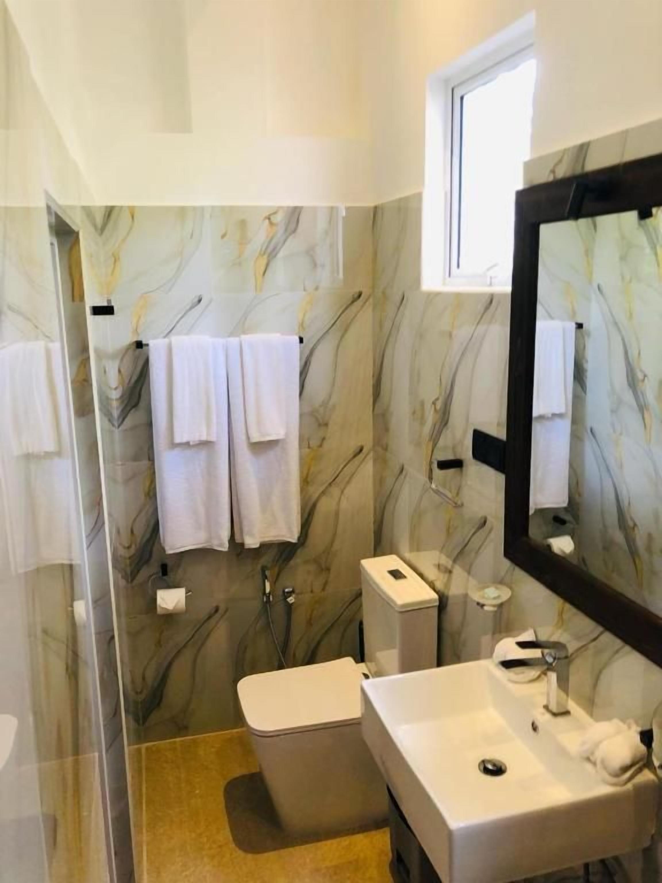 Un baño con pared de mármol, un lavamanos blanco, un inodoro y una cabina de ducha de vidrio.