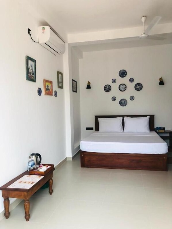 A bedroom with a bed, a small table with a kettle, and wall decorations including plates and pictures.