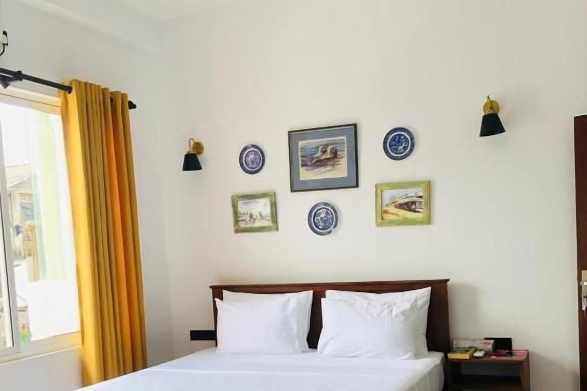 A bedroom with a bed, bedside tables, a nightstand, a window with curtains, and wall-mounted lamps.