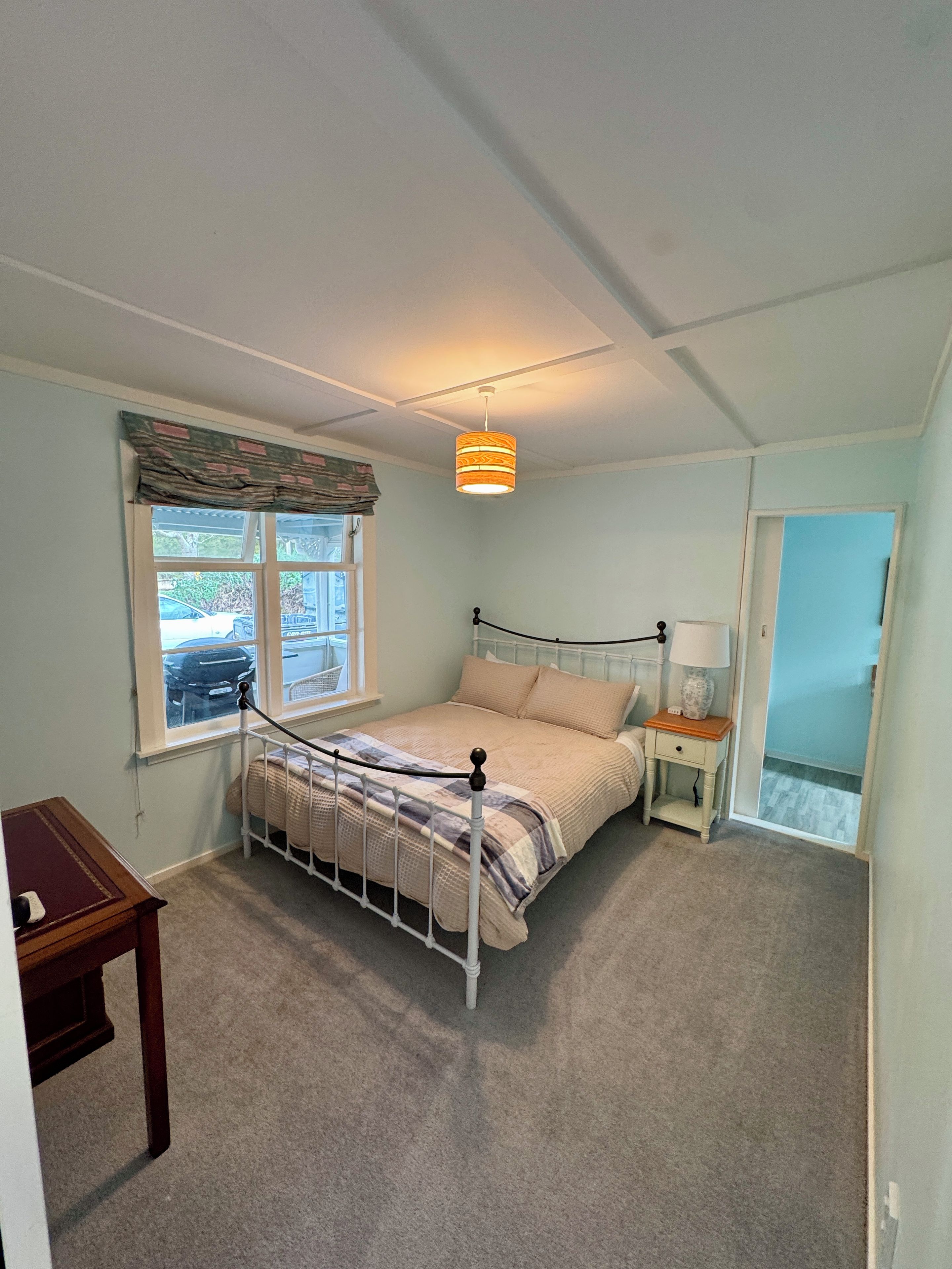 Een slaapkamer met een bed, nachtkastje, lamp, raam en deur.