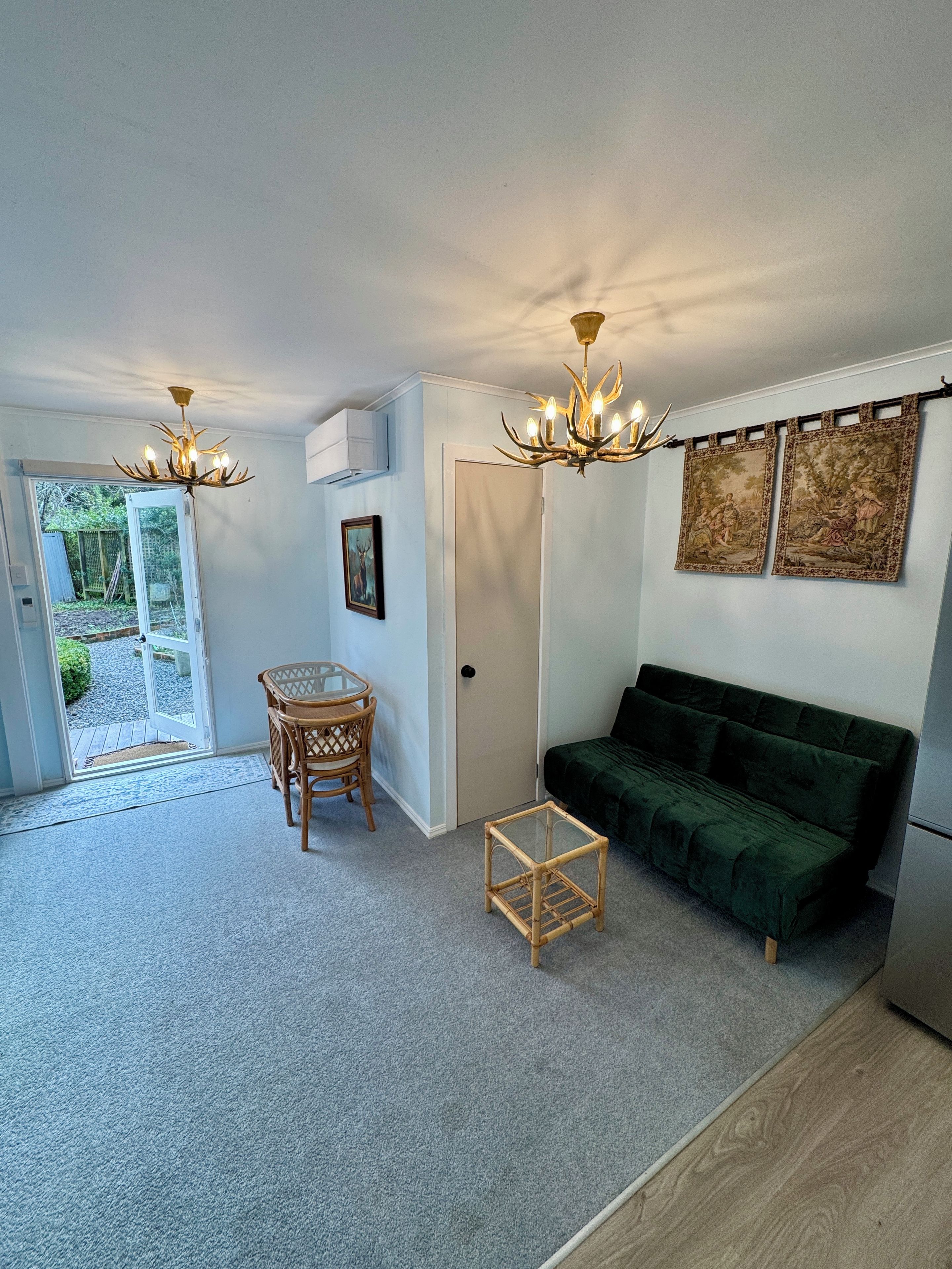 A living room with a green sofa, a small table, a chair, two chandeliers, and a door leading outside.