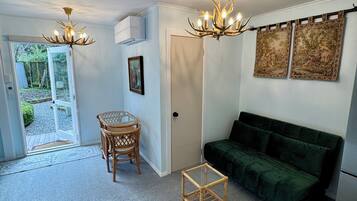 A living room with a green sofa, a small table, a chair, two chandeliers, and a door leading outside.