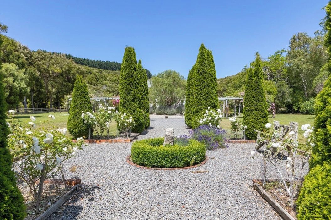 A garden with a gravel path, neatly trimmed hedges, and a variety of flowering plants.