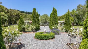A garden with a gravel path, neatly trimmed hedges, and a variety of flowering plants.