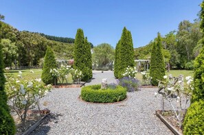 A garden with a gravel path, neatly trimmed hedges, and a variety of flowering plants.