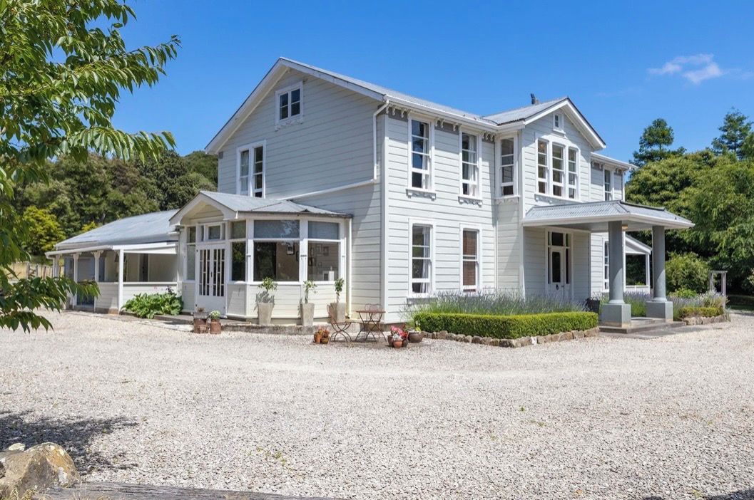 A two-story house with a covered porch, a gravel driveway, and a well-maintained garden.