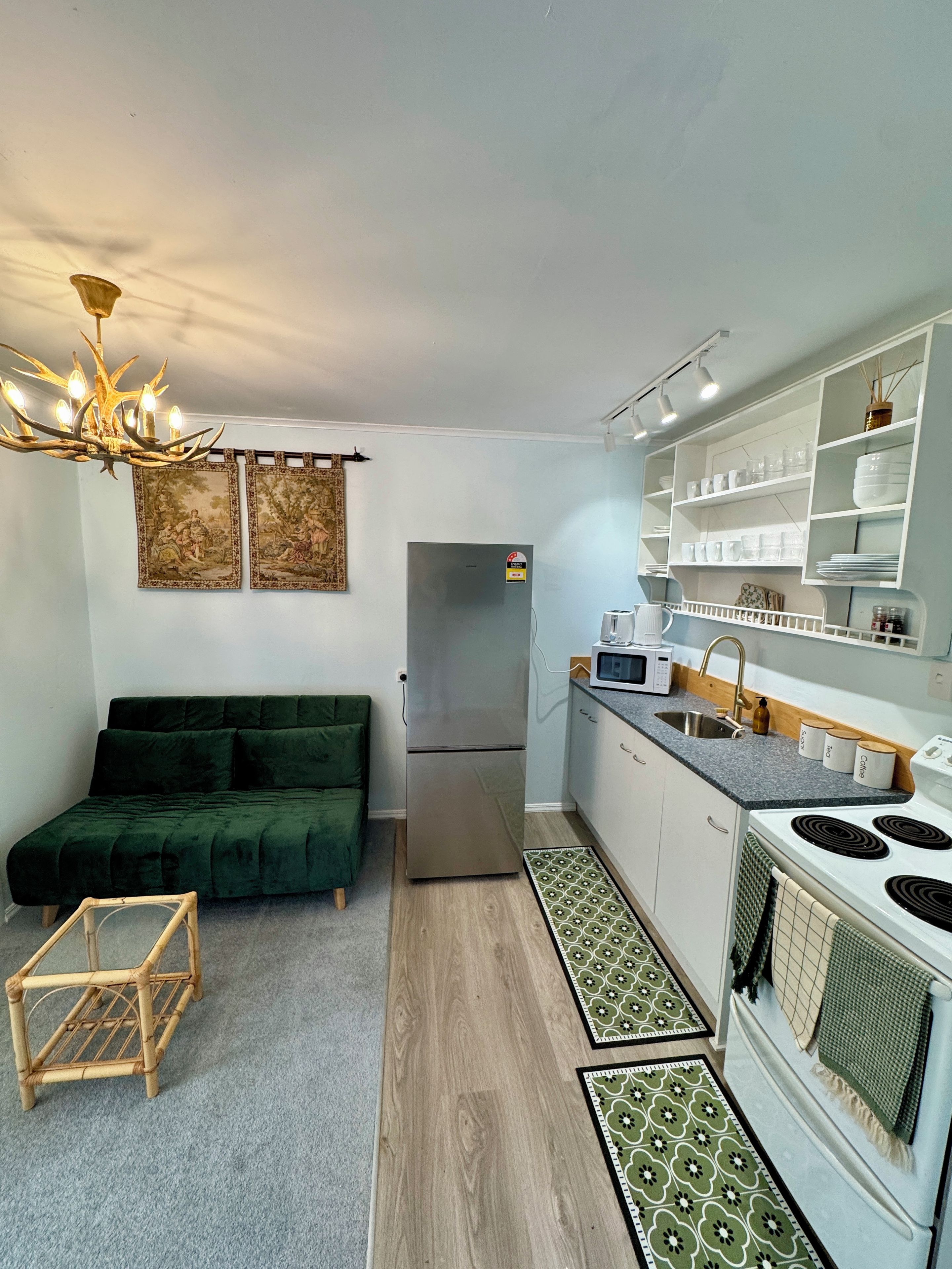 A compact kitchen with a refrigerator, microwave, and stove. There is a green sofa and a small wooden table.