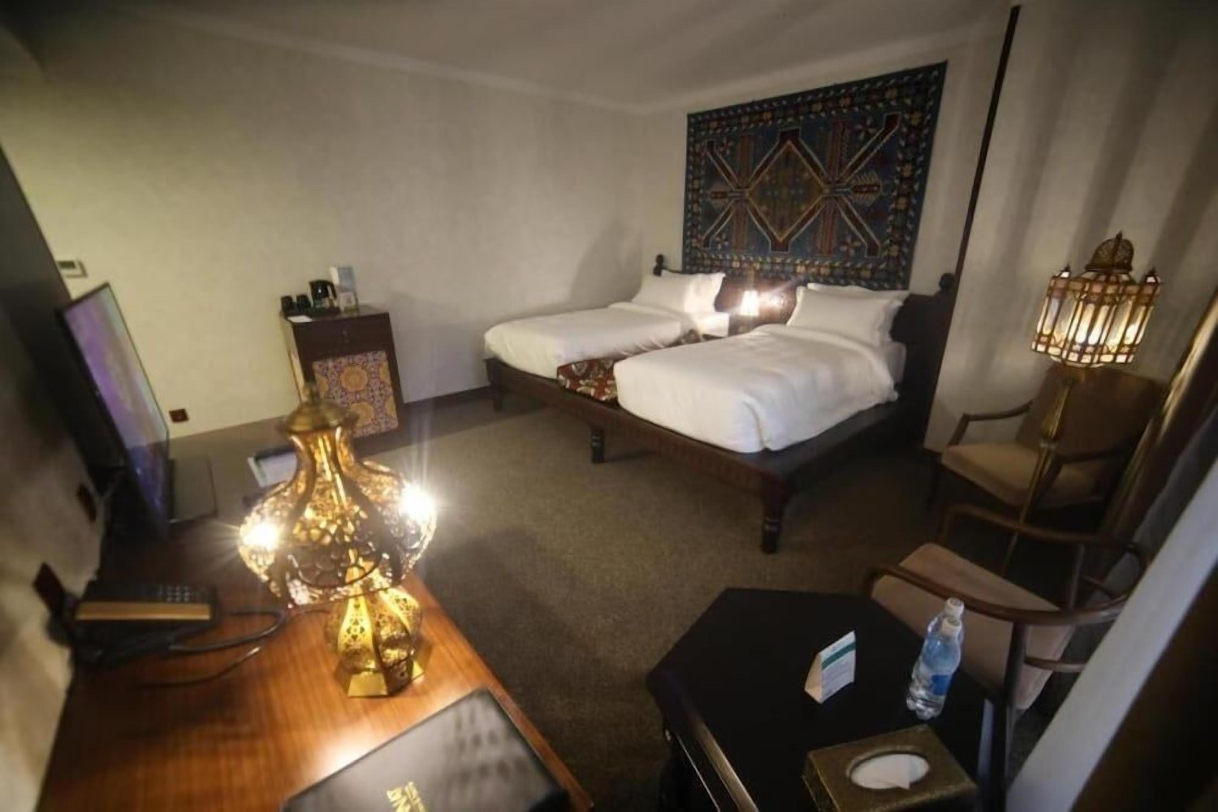 Ett hotellrum med en säng, ett sängbord, en lampa och en väggbonad.