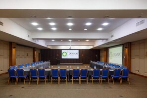 Un salón de conferencias con una larga mesa, sillas azules y una pantalla con la marca JANNAT.